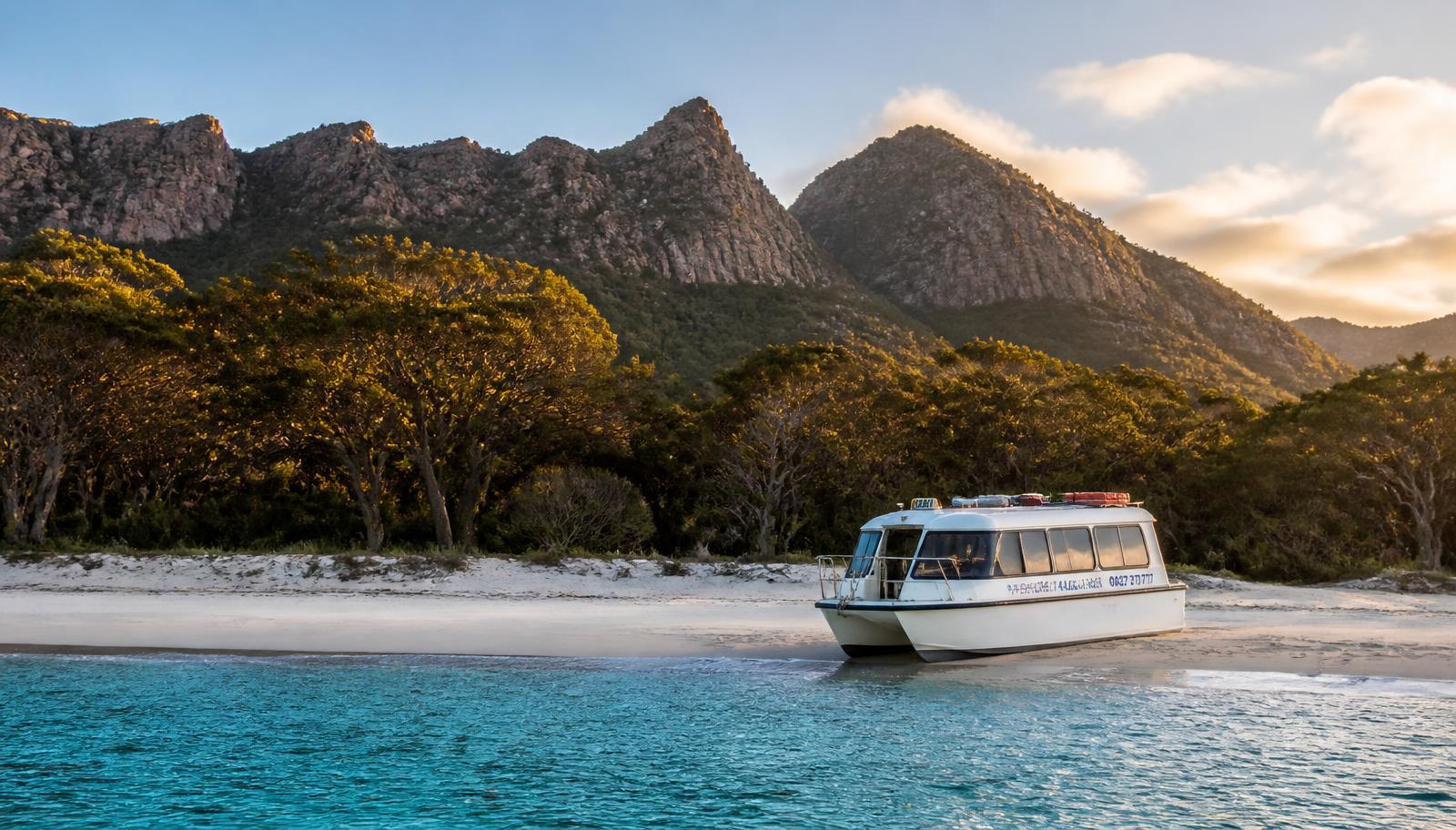 Water taxi nosed onto the white sand of Wineglass Bay with the granite Hazards peaks behind, Freycinet Peninsula Tasmania
